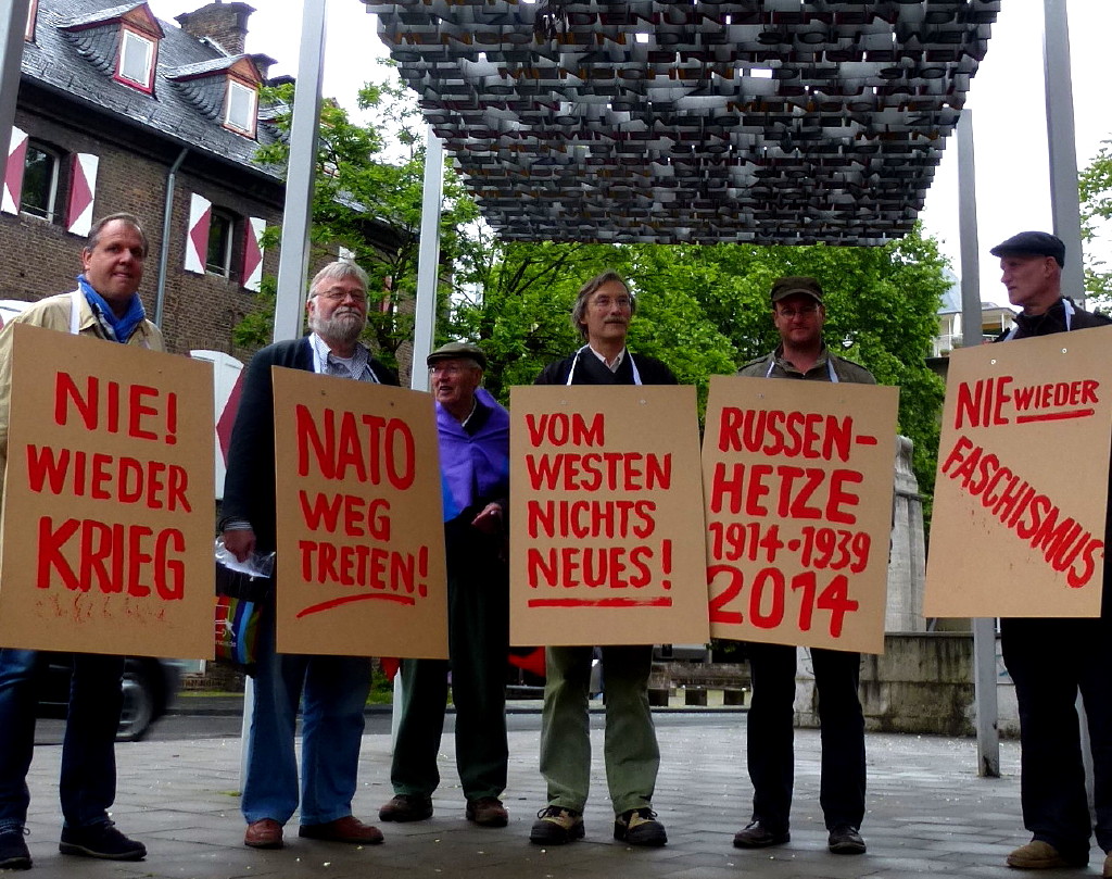 Demonstranten mit Umhängeschildern: »Nie wieder Krieg! NATO wegtreten! Vom Westen nichts Neues! Nie wieder Faschismus! Russen-Hetze 1914-1939 und 2014«.
